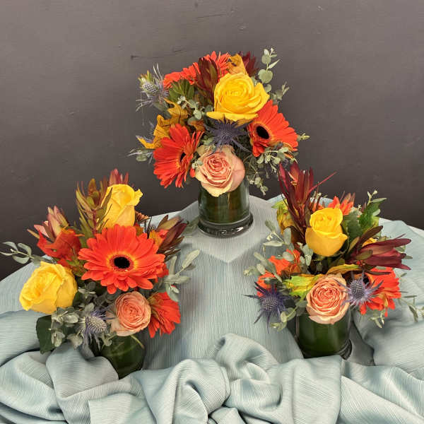Three small floral arrangements in green vases with yellow and orange blooms