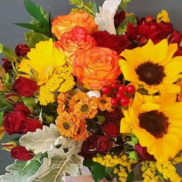 Bouquet of yellow sunflowers, orange and red roses, and orange mums with silvery foliage.