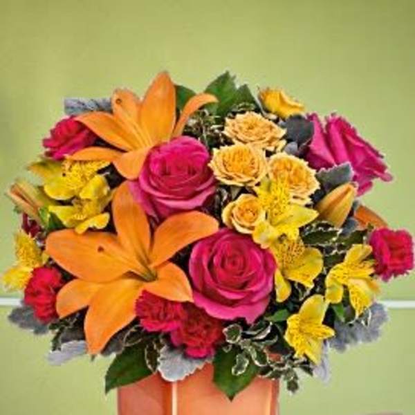 Bright bouquet of orange lilies, pink roses, and yellow flowers in a square vase