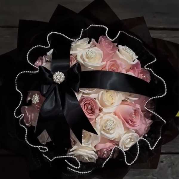 Bouquet of pink and white roses wrapped in black paper with a satin bow