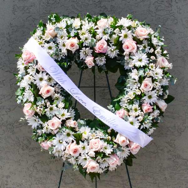 Heart-shaped floral wreath with pink roses and white daisies on a stand