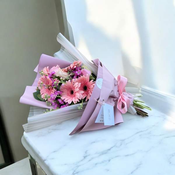 Pink gerbera daisy bouquet wrapped in lavender paper with a ribbon