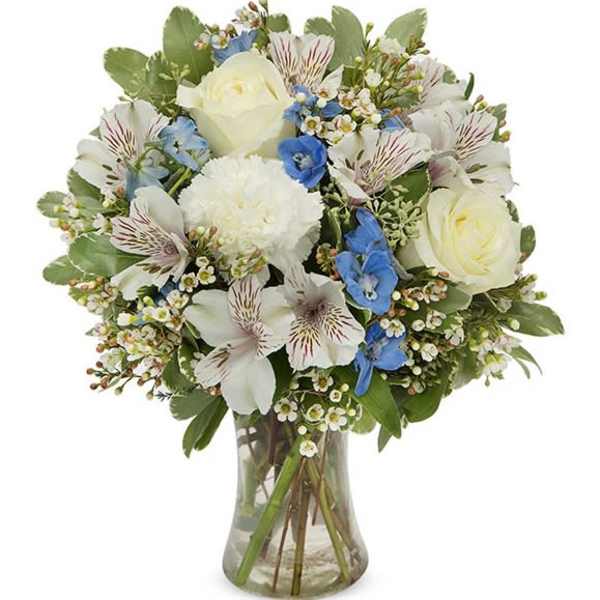 Vase arrangement of white roses, carnation, alstroemeria and blue flowers in a clear glass vase
