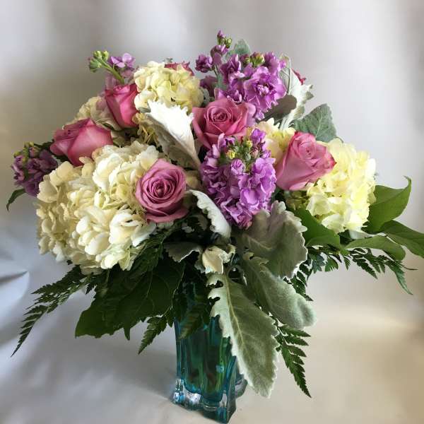Pink roses and pale hydrangeas arranged in a blue glass vase