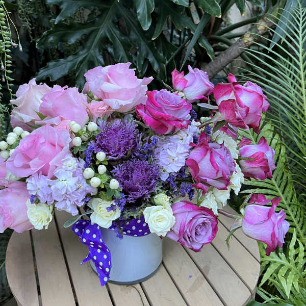 Pink and white roses arranged in a white bucket with a purple ribbon