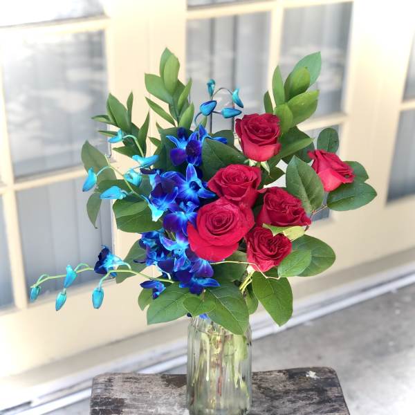 Bouquet of red roses and blue orchids in a glass vase