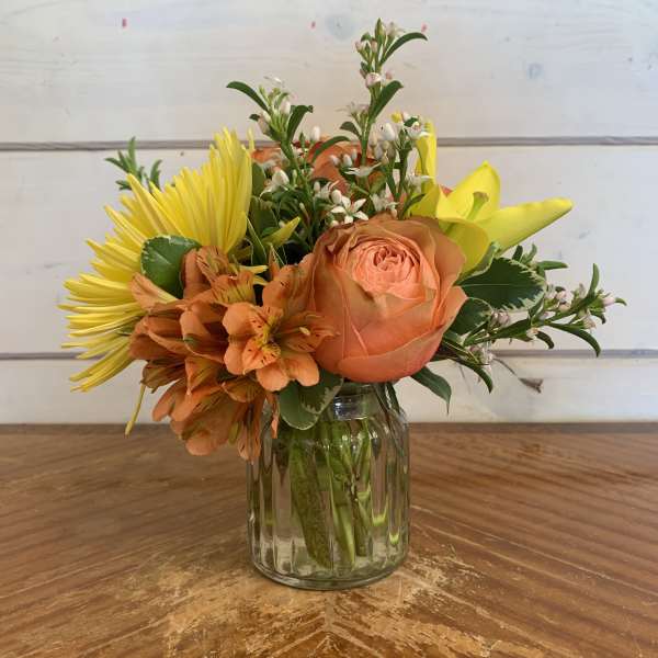 Mixed bouquet of orange, yellow, and white flowers in a glass jar