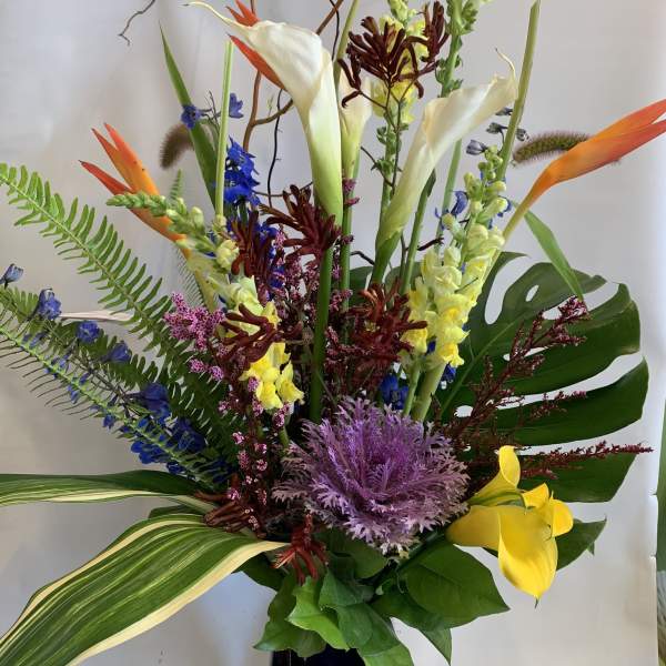 Tall tropical bouquet with calla lilies, orchids, and bird-of-paradise in a dark vase