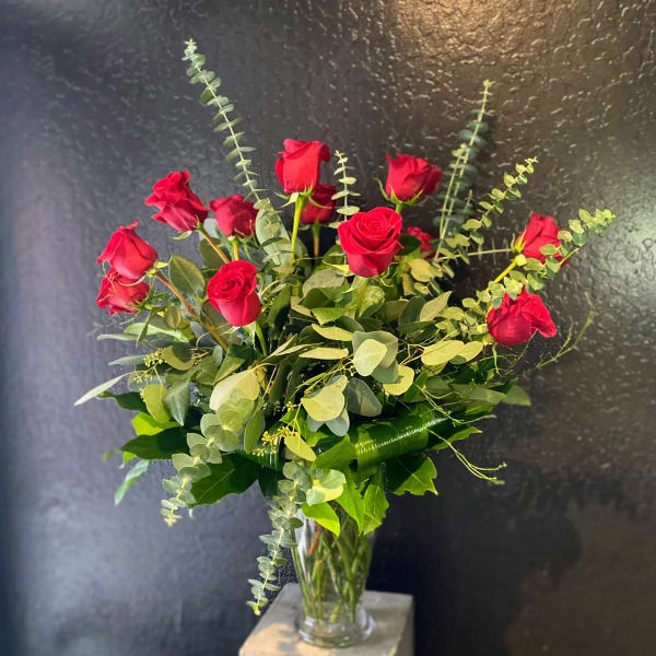 Red roses arranged in a clear glass vase with eucalyptus foliage