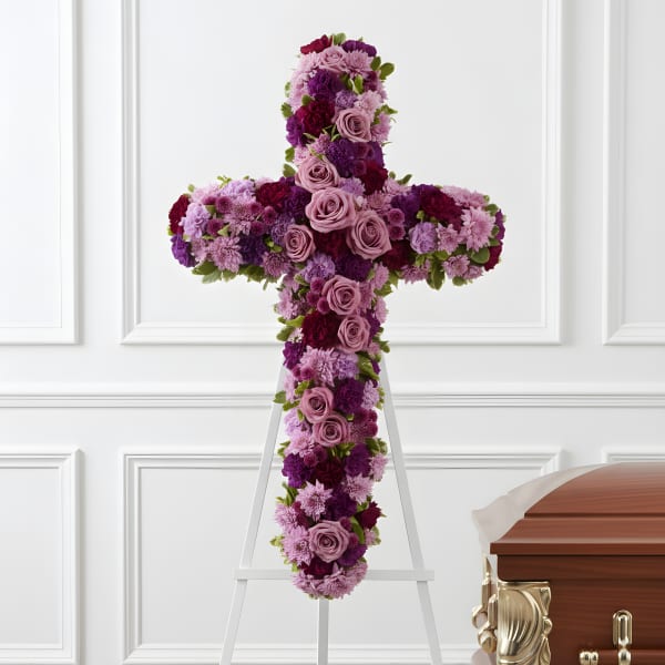 Purple and pink floral cross on a white easel beside a casket