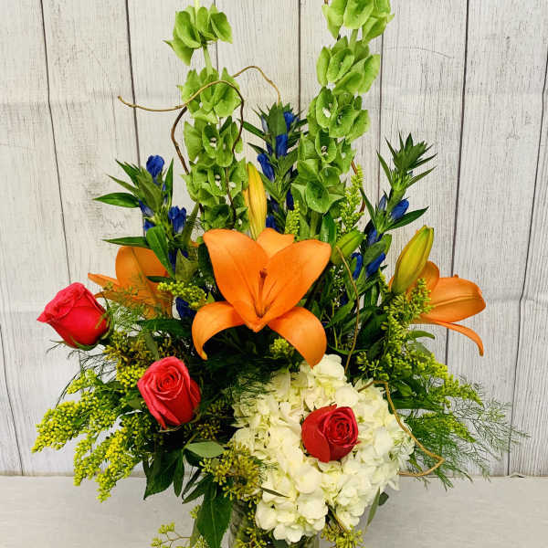 Tall mixed bouquet with orange lilies, red roses, and white hydrangeas in a glass vase