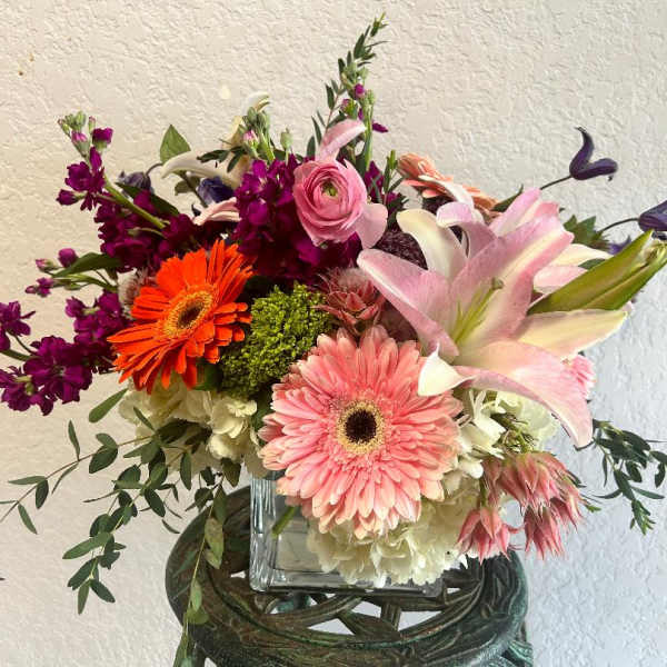 Mixed bouquet with pink lilies, gerbera daisies, and purple blooms in a glass vase
