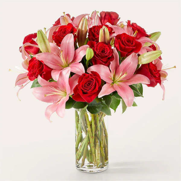 Tall clear vase of red roses and pink lilies arranged in a rounded bouquet