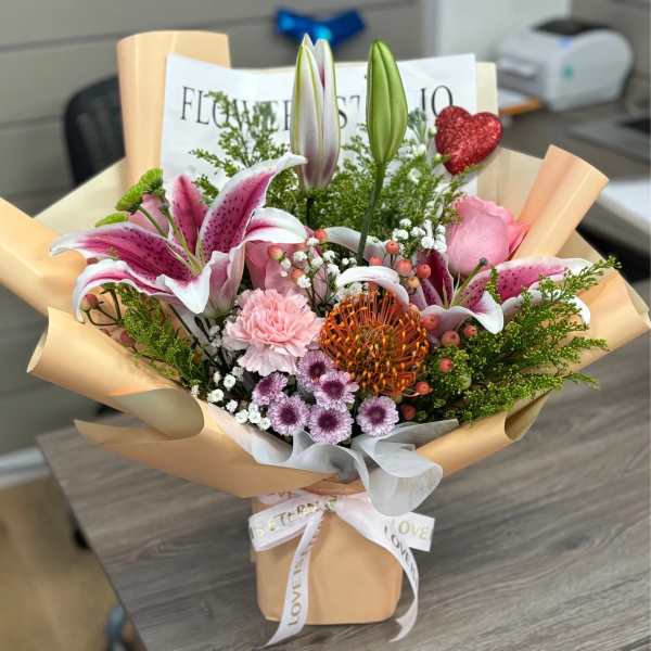 Bouquet of pink lilies, roses, and mixed flowers wrapped in peach paper