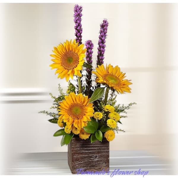 Tall sunflower and yellow mum arrangement with purple accents in a square wooden vase