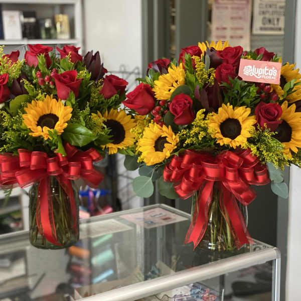 Two bouquets of red roses and sunflowers in glass vases with red bows