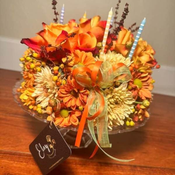 Orange and yellow floral arrangement with striped candles and a ribbon bow in a glass bowl