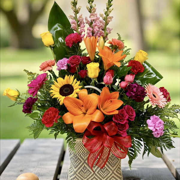 Colorful mixed flower arrangement in a woven basket with a red ribbon