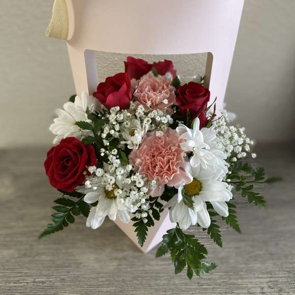 Pink gift box with red roses, pink carnations, and white daisies