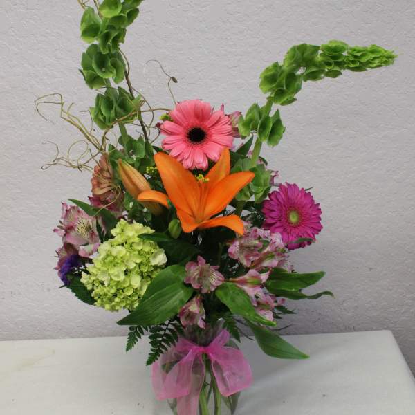 Mixed bouquet with orange lily, pink gerbera daisies, and green hydrangea in a glass vase
