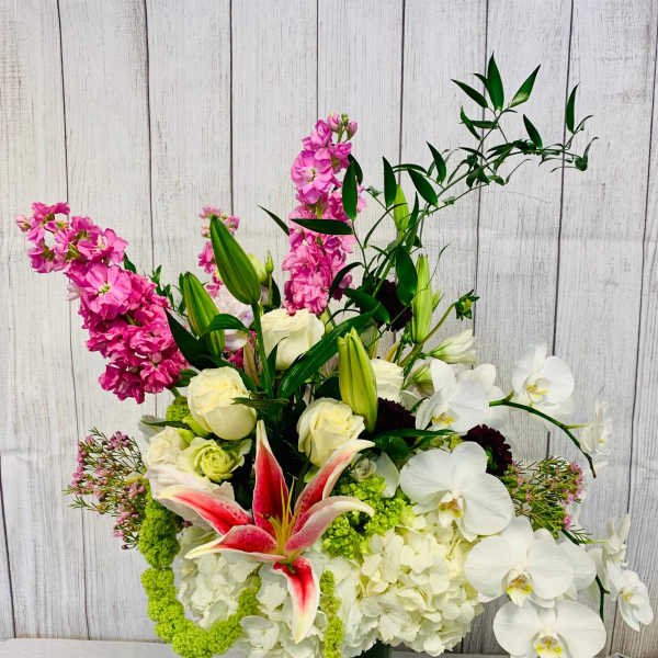 Tall mixed floral arrangement in a glass vase with white orchids and pink lilies
