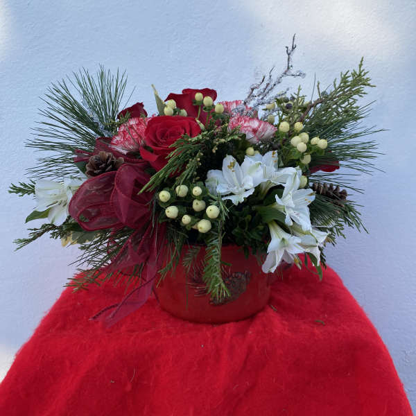 Red roses and white flowers in a red container with pine accents
