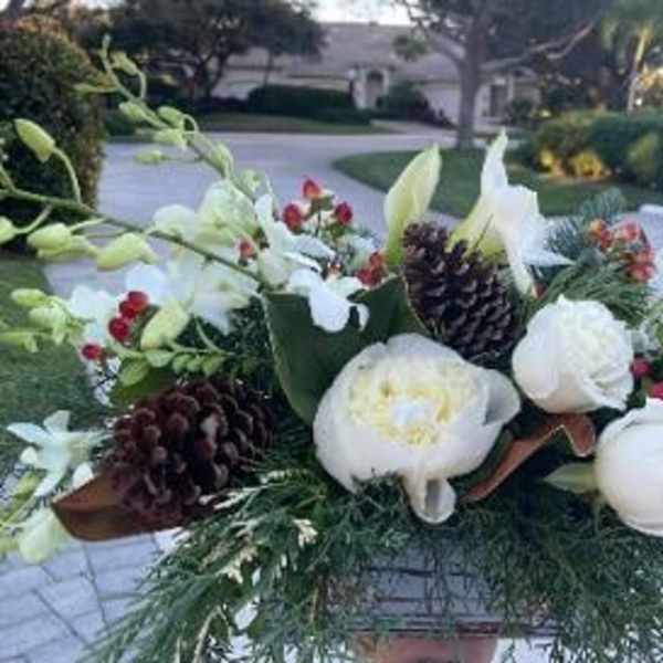 White floral arrangement with pinecones and red berries in a container