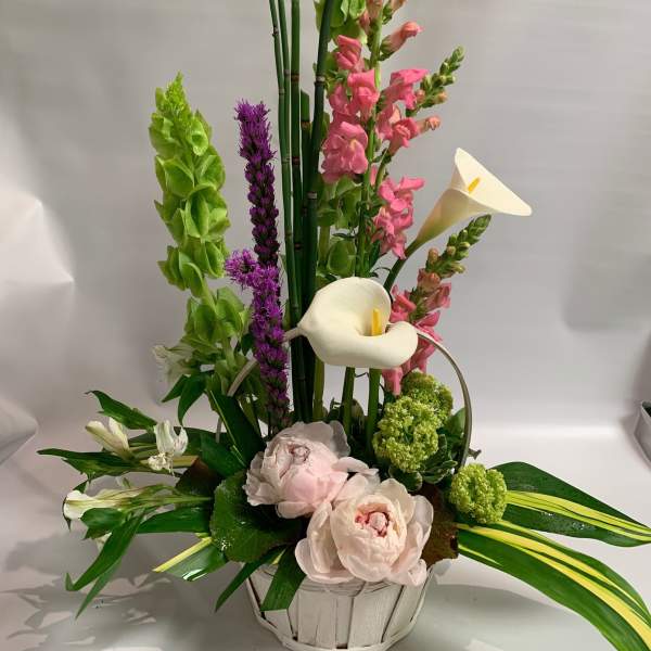 Tall floral arrangement with white calla lilies, pink blooms, and green spikes in a white basket
