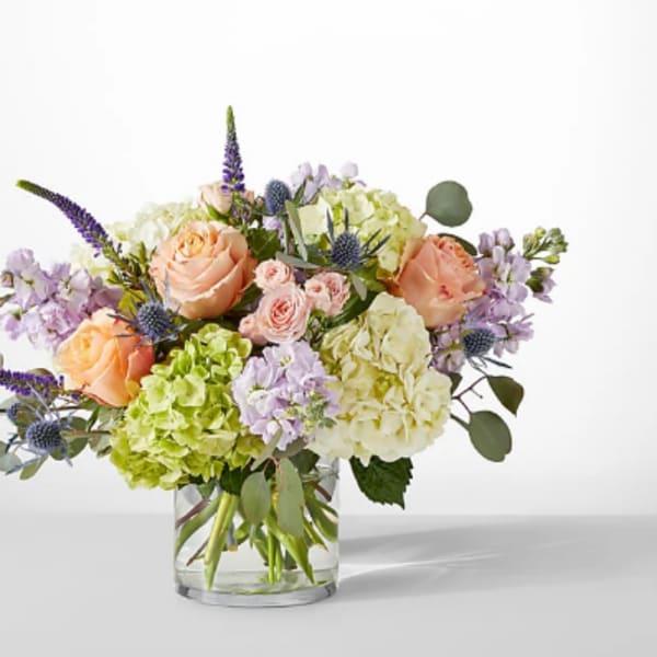 Peach roses and hydrangeas in a clear glass vase with lavender accents
