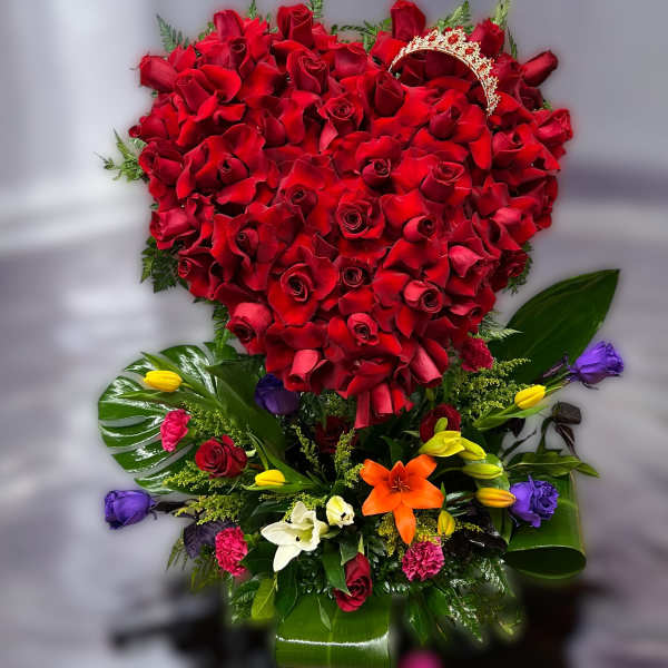 Tall arrangement with a heart of red roses above mixed colorful blooms and a gold tiara accent.