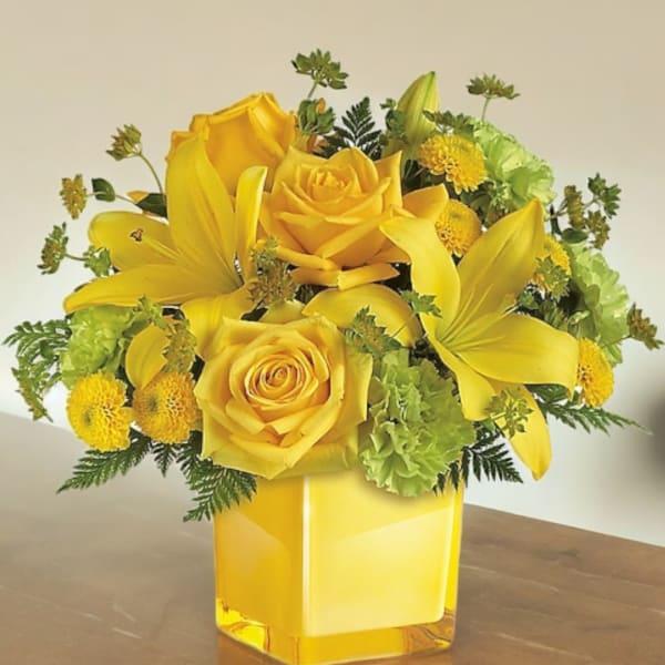 Yellow roses and lilies arranged in a square glass vase