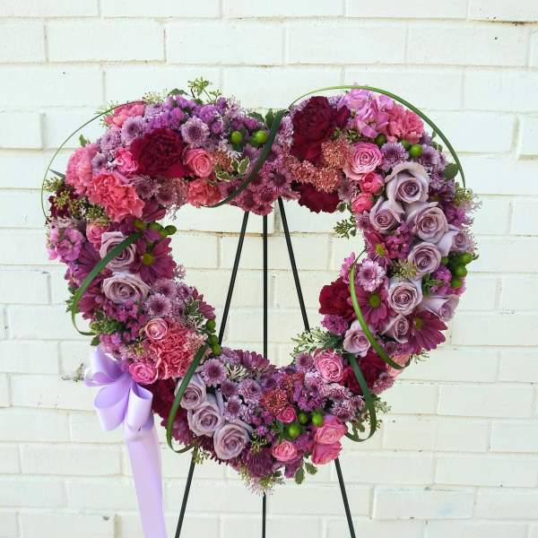 Heart-shaped floral wreath in pink, purple, and lavender tones on a stand