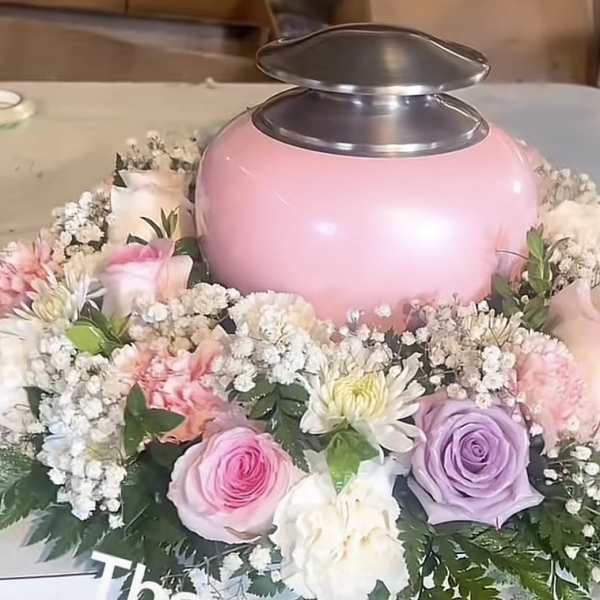 Pink urn surrounded by pastel roses and white filler flowers