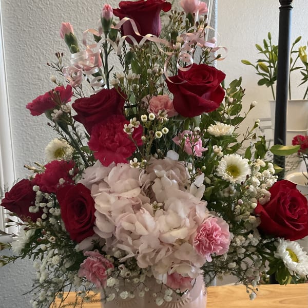 Pink and red floral arrangement in a pale vase with ribbon accents