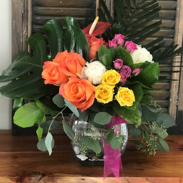 Colorful rose bouquet in a glass vase with tropical leaves