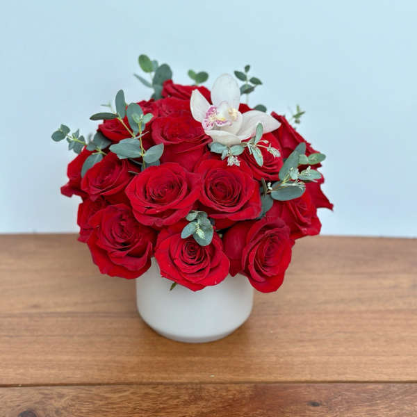 Red roses in a white vase with a white orchid bloom
