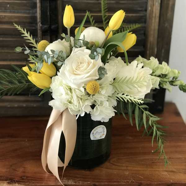 White roses and hydrangeas with yellow tulips in a black vase