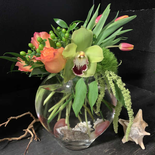 Tropical floral arrangement in a round glass vase with orchids and tulips