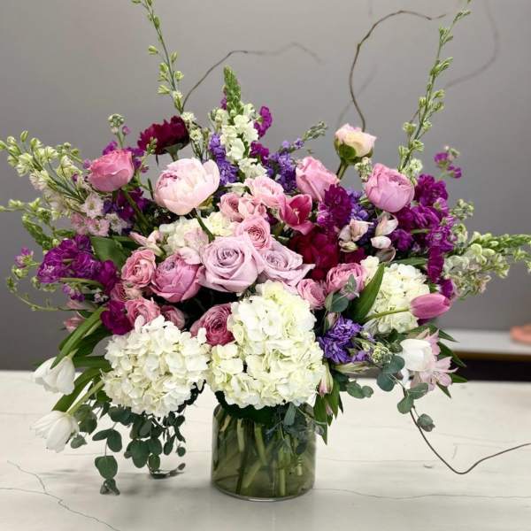 Mixed pink, purple, and white flowers arranged in a glass vase