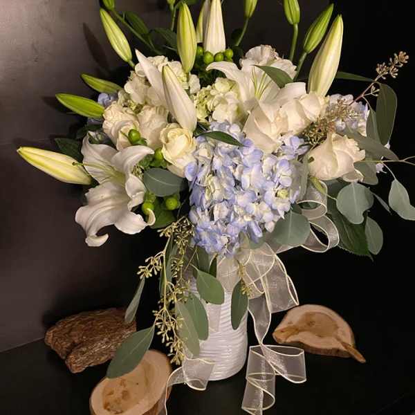 White lilies and pale blue hydrangeas in a white vase with ribbon
