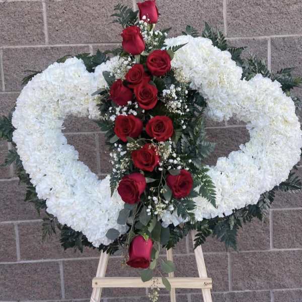 Heart-shaped white floral wreath with red roses on an easel