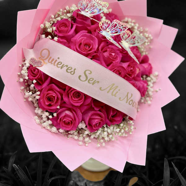 Bouquet of bright pink roses with baby's breath, pink wrapping, and a ribbon with Spanish proposal text