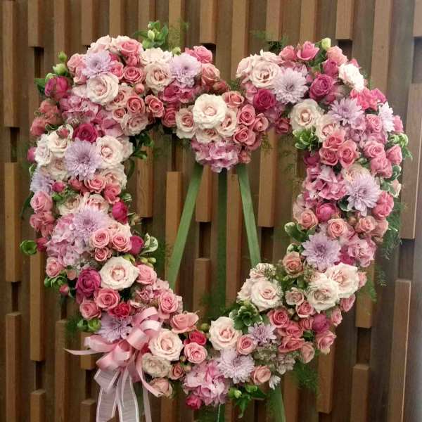 Heart-shaped floral wreath of pink and white roses with a ribbon bow
