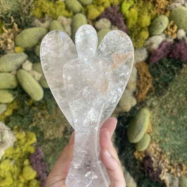 Hand holding a clear crystal angel figurine in front of a moss wall