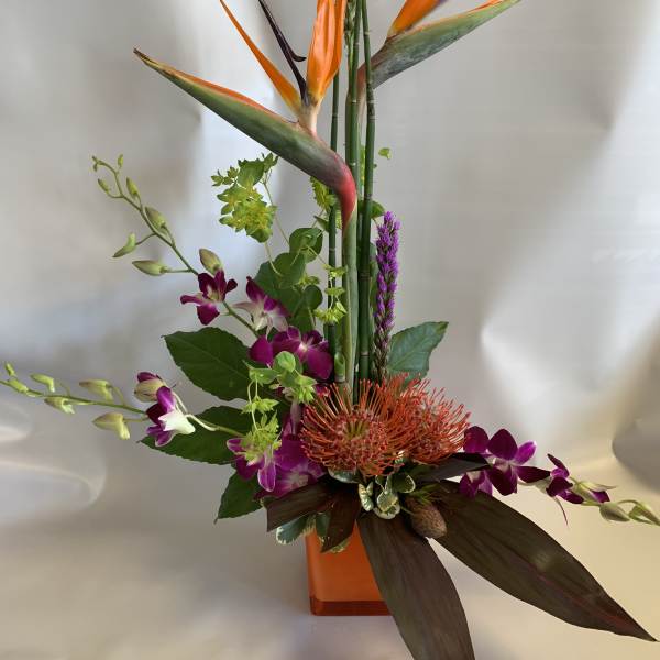 Tall tropical arrangement with orange bird of paradise and purple orchids in a vase