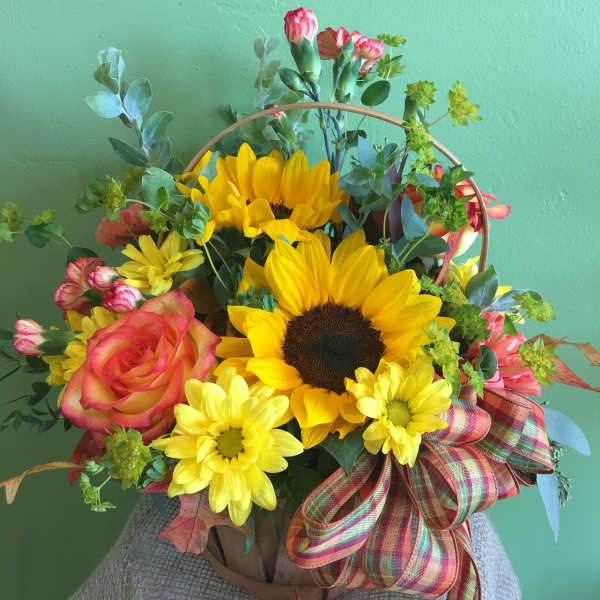 Basket arrangement with sunflowers, roses, and daisies tied with a plaid ribbon
