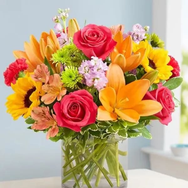 Bright mixed bouquet of roses, lilies, and sunflowers in a glass vase