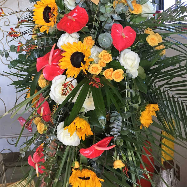Tall floral standing spray with sunflowers, roses, and red anthuriums