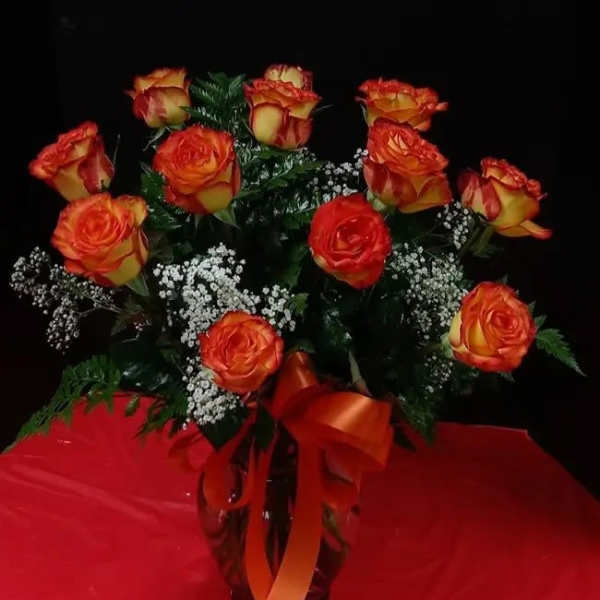Bouquet of orange and yellow roses in a glass vase with red ribbon