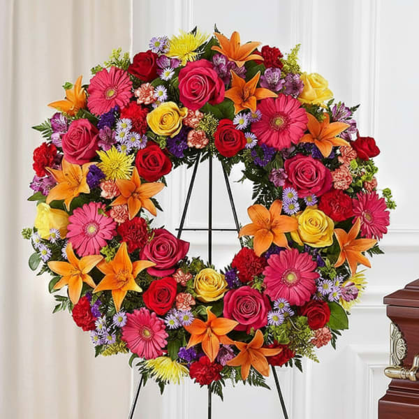 Colorful floral wreath on a black stand with roses, lilies, and daisies